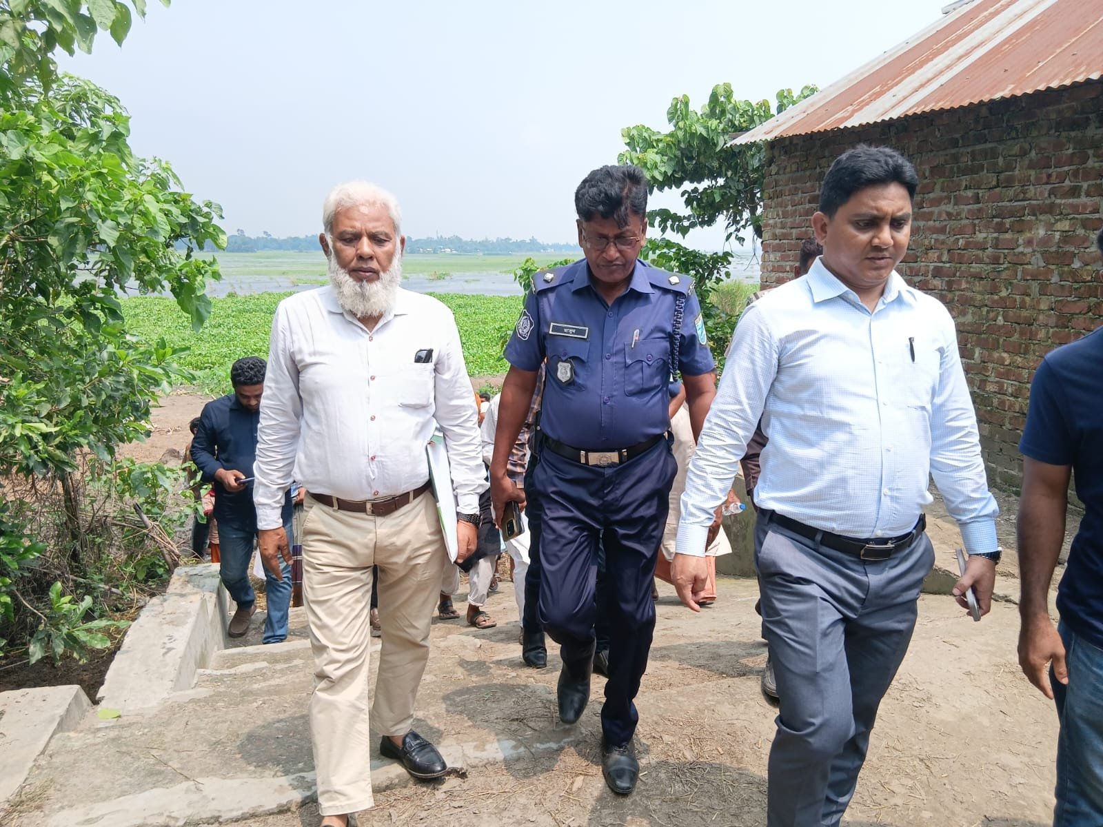 Officials walking a field path with a police officer.